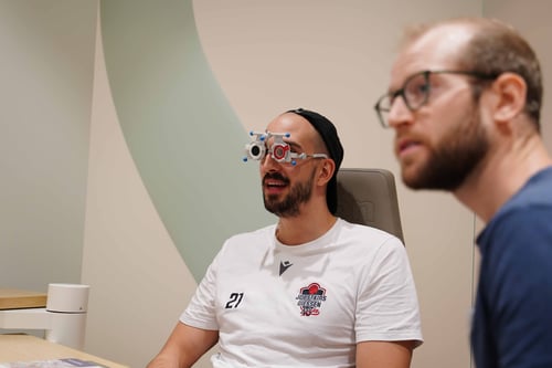 Mann sitzt während eines Sehtests mit Messbrille in einem Untersuchungsraum