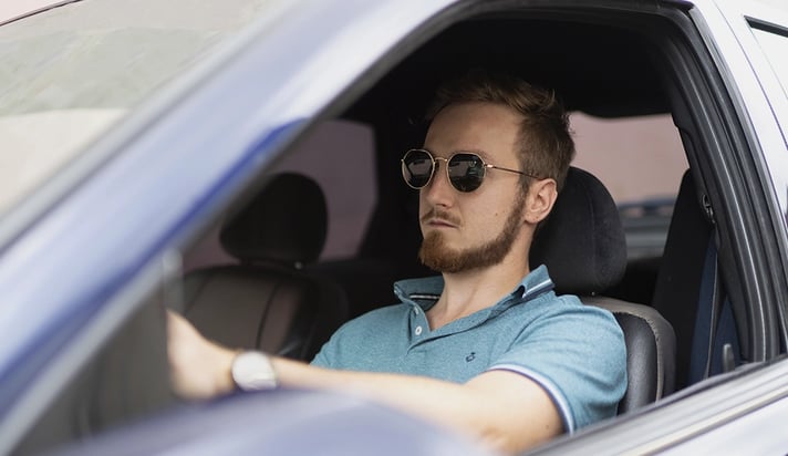 Eine Person sitzt am Steuer eines Autos und trägt eine Sonnenbrille