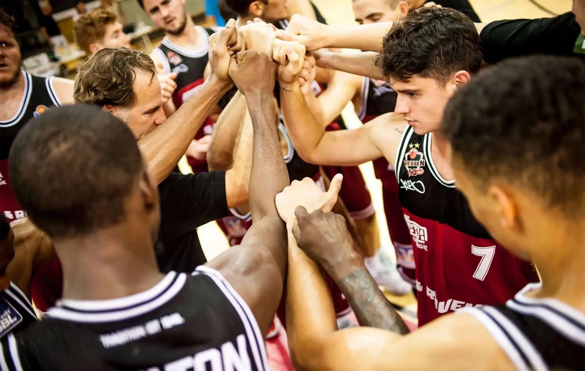 Mehrere Basketballspieler strecken Hände zur Mitte für einen Mannschafts-Huddle.