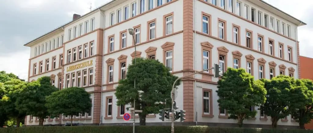 Mehrstöckiges Schulgebäude mit Aufschrift „LIEBIGSCHULE" und Bäumen davor.