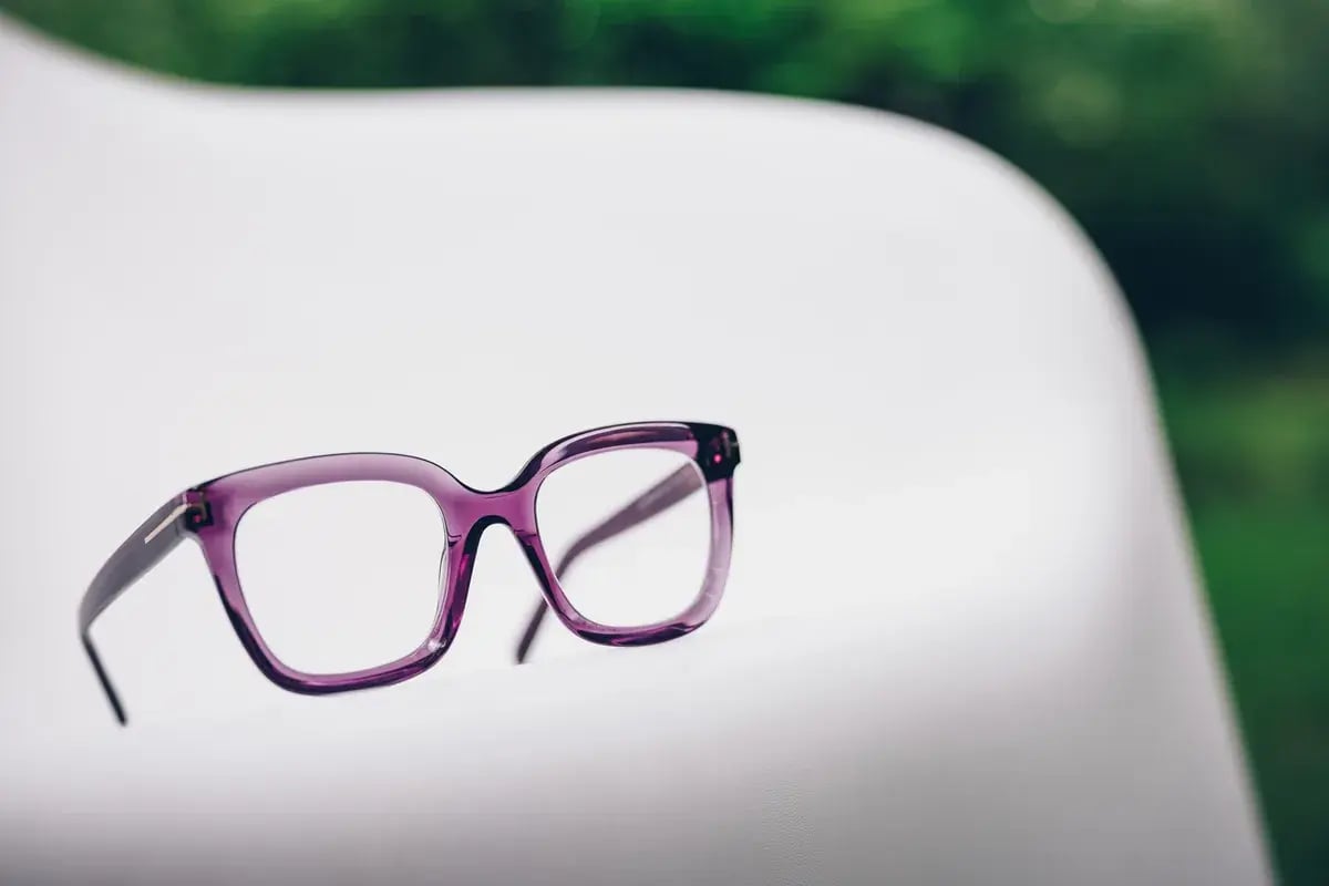 Lila Damenbrille liegt auf einem weißen Stuhl als Freisteller-Aufnahme