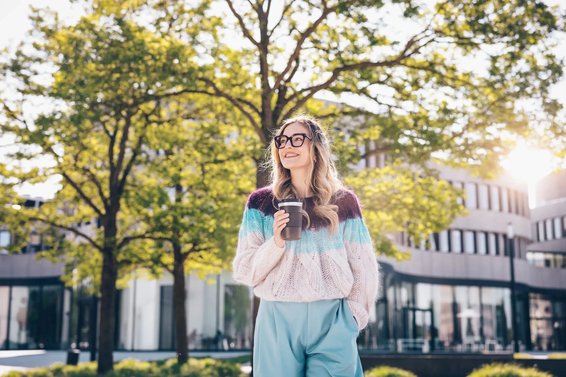 Frau mit Brille hält eine Kaffeetasse im Freien bei Sonnenschein