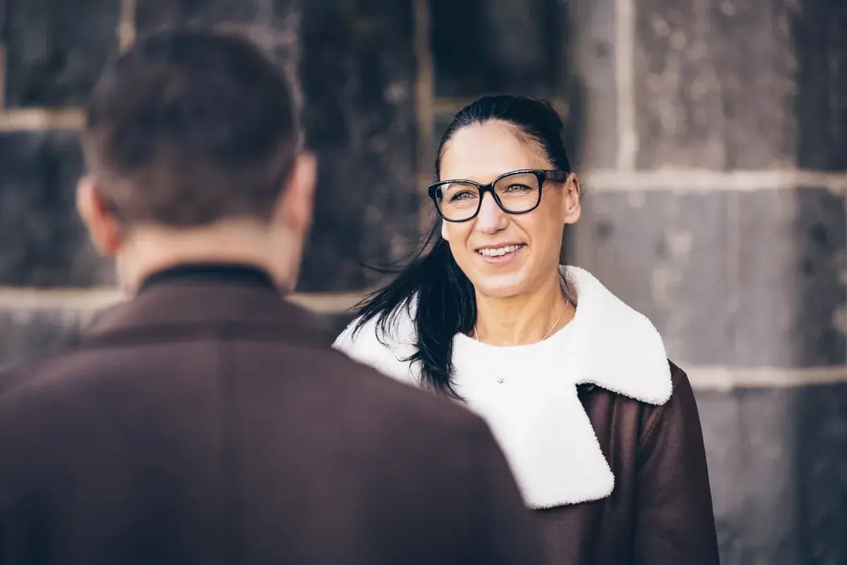 Frau mit Brille führt ein Gespräch mit einer anderen Person im Freien