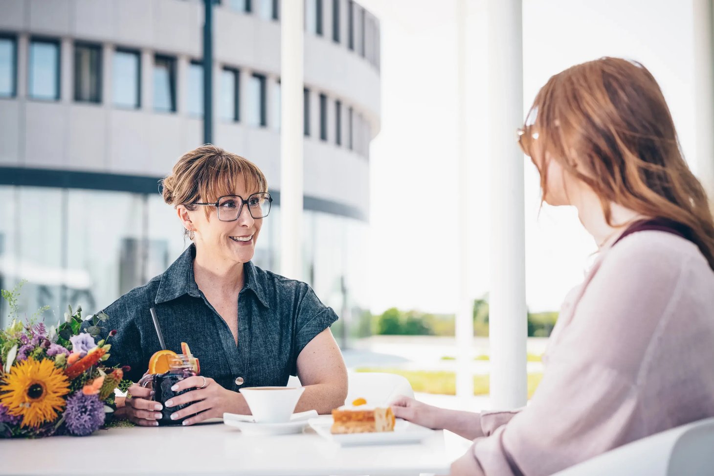 Zwei Frauen mit Brillen unterhalten sich auf einer Terrasse im Freien