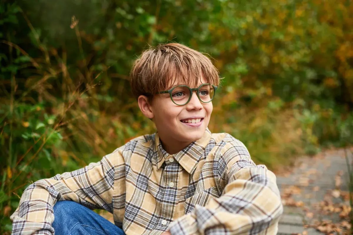Junge mit Brille sitzt im Wald