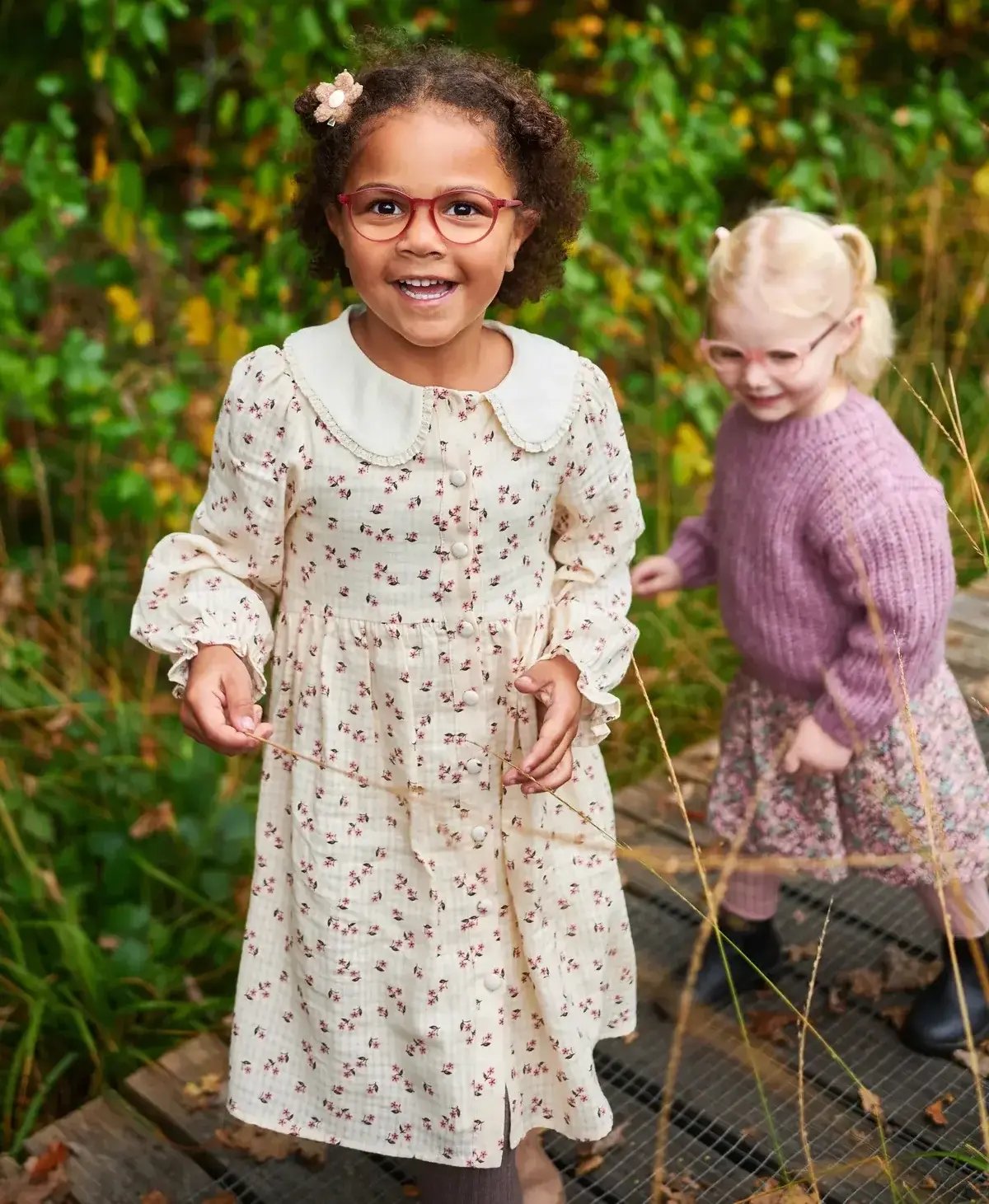 Mädchen mit Kinderbrille steht in einem herbstlichen Wald