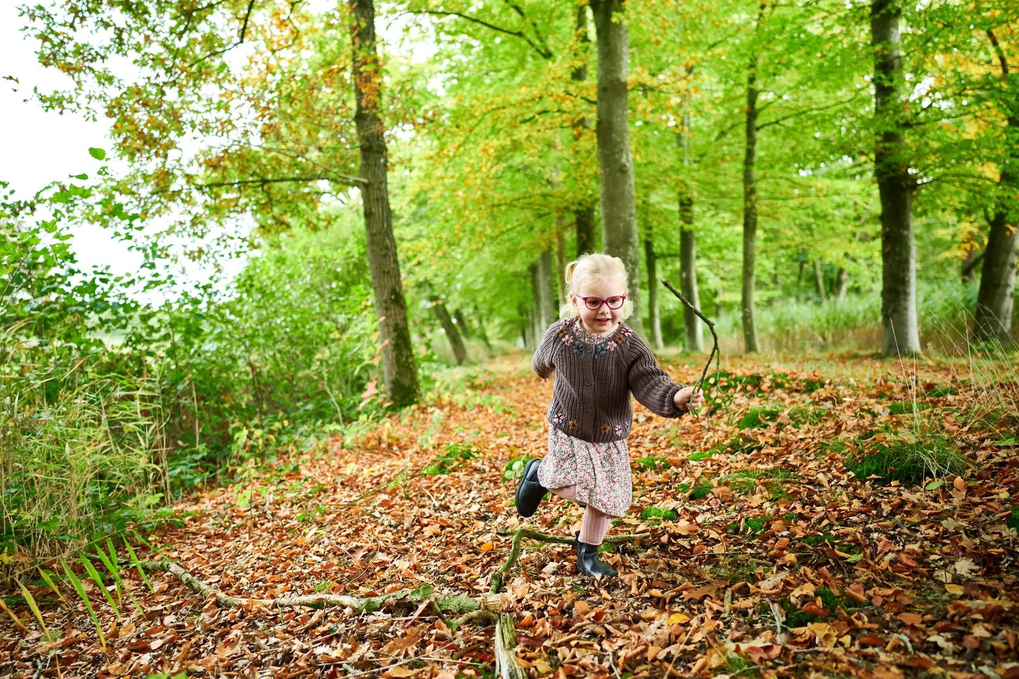 Mädchen mit Kinderbrille spielt in einem herbstlichen Wald