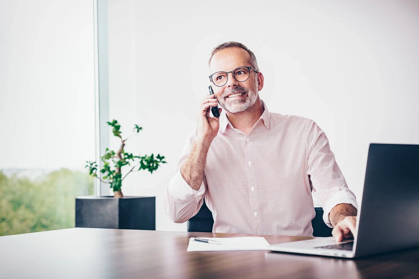 Mann mit Brille telefoniert und arbeitet an einem Büroschreibtisch