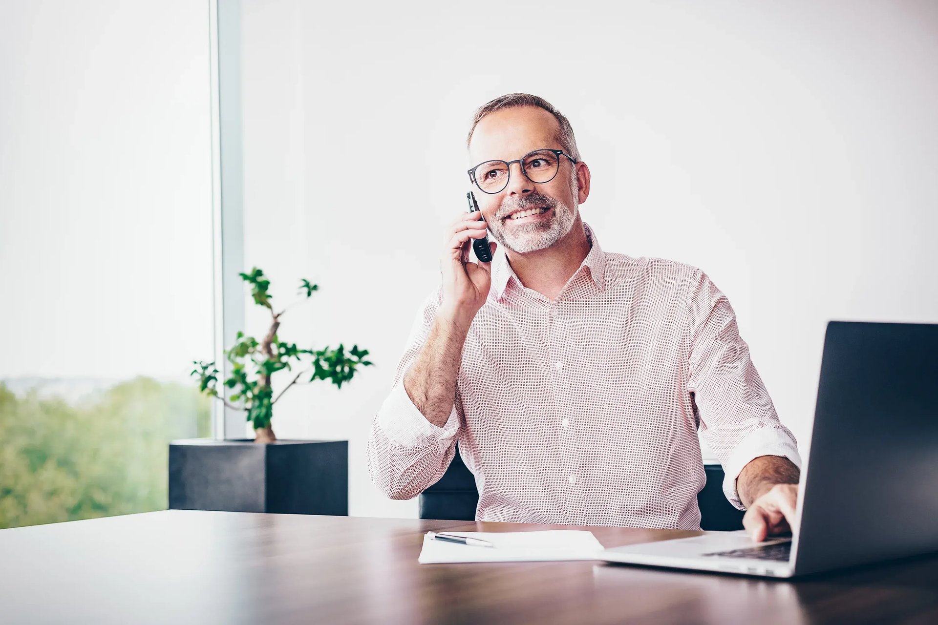 Mann mit Brille telefoniert und arbeitet an einem Büroschreibtisch
