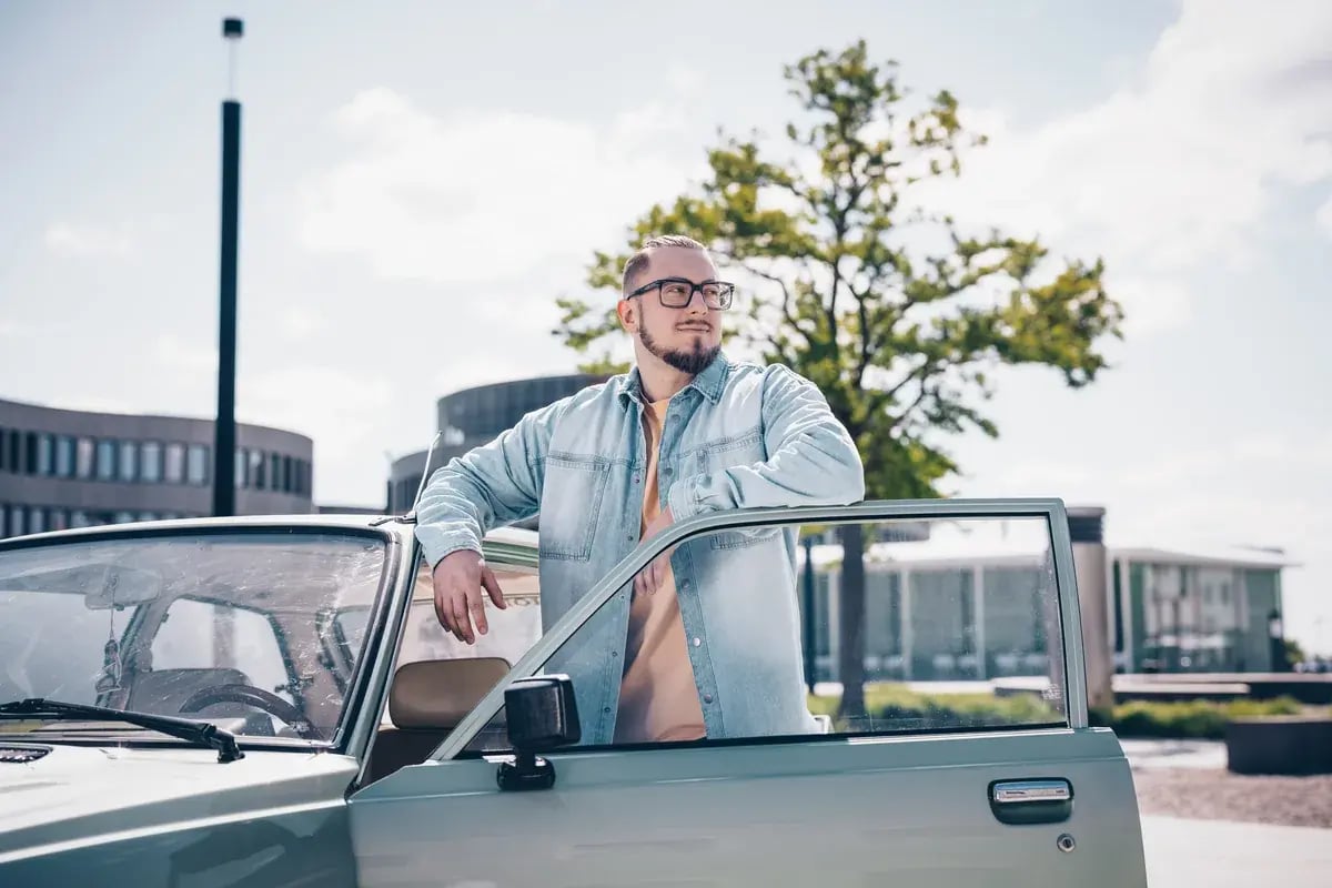 Mann mit Brille steht an einem Auto und guckt in die Ferne