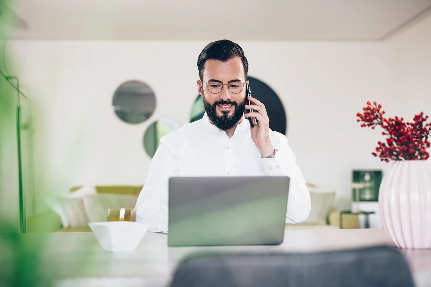 Mann mit Brille telefoniert und schaut dabei auf einen Laptop