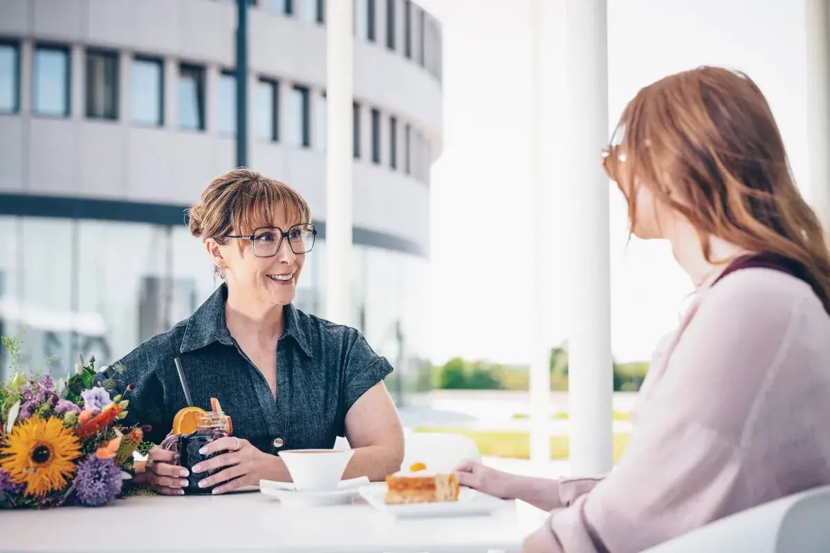 Zwei Frauen mit Brillen unterhalten sich auf einer Terrasse