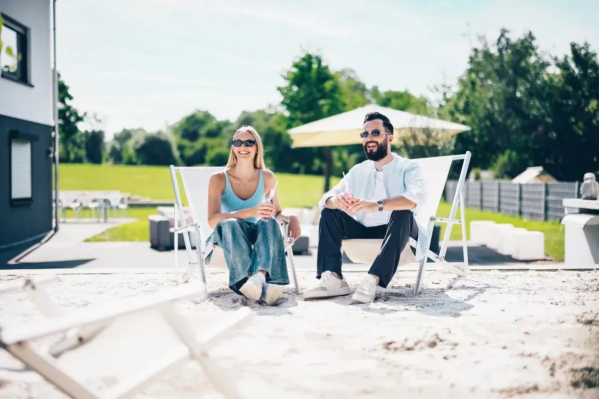 Paar mit Sonnenbrillen liegt entspannt in Liegestühlen im Freien