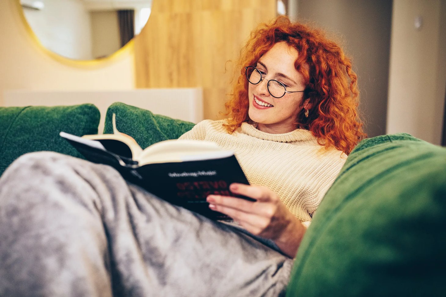 Frau mit Lesebrille liegt auf einer Couch und liest ein Buch