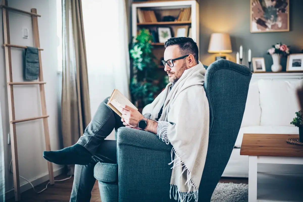 Mann mit Lesebrille sitzt im Sessel und liest ein Buch