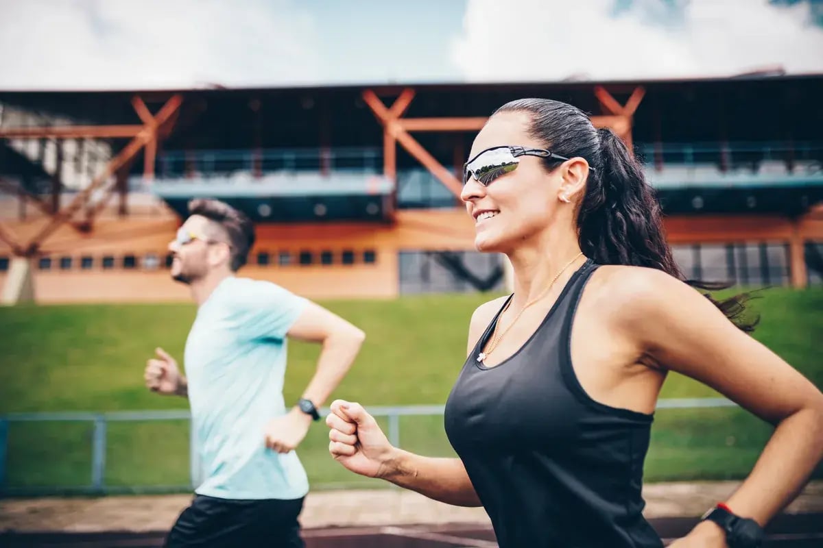Frau mit Sportbrille und Mann laufen lächelnd auf einer Stadionbahn