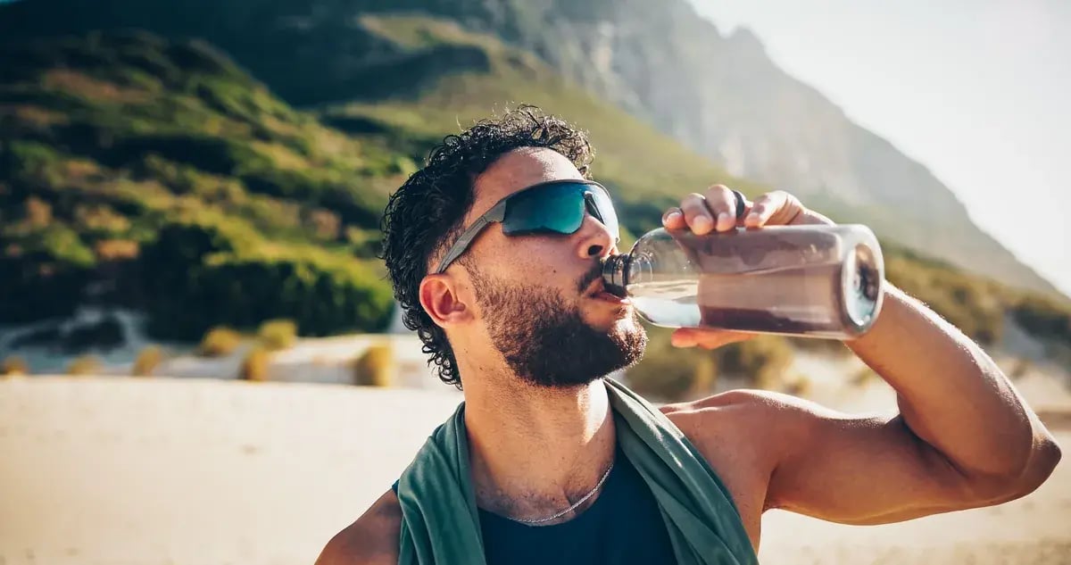 Mann mit Sportbrille steht vor einer Gewässer- und Berglandschaft