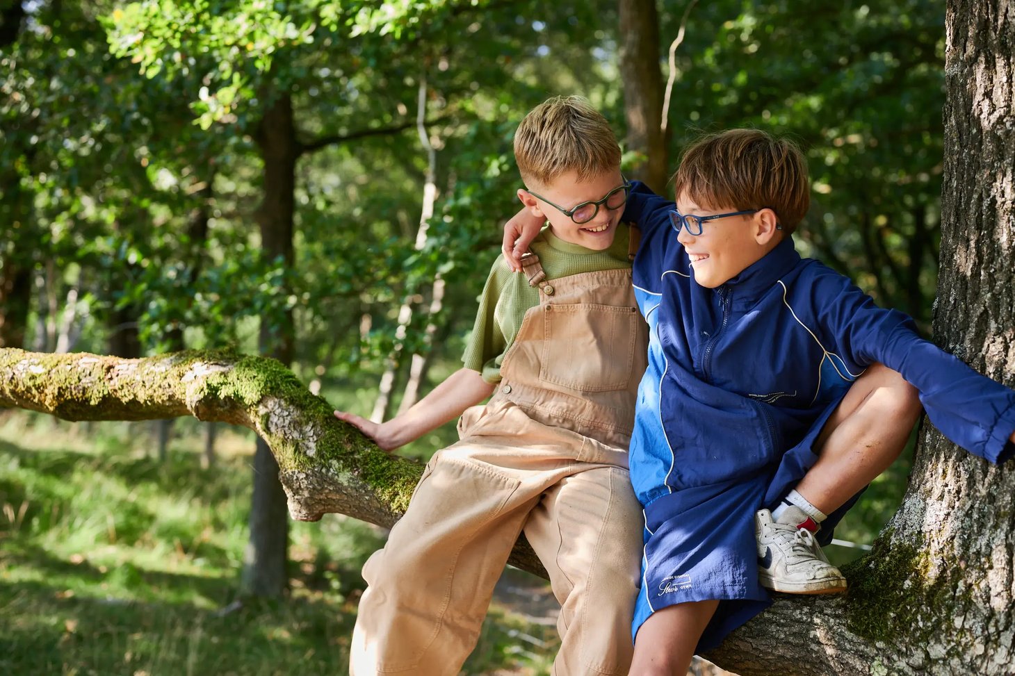 Zwei Jungen mit Brillen sitzen auf einem Baumstamm im sonnigen Wald