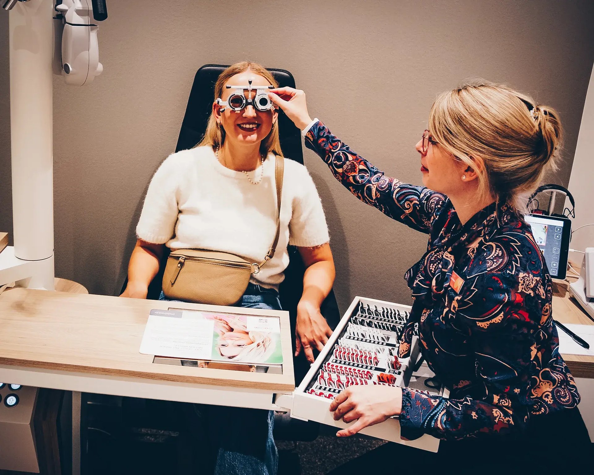 Optikerin setzt einer sitzenden Patientin eine Probierfassung für den Sehtest auf