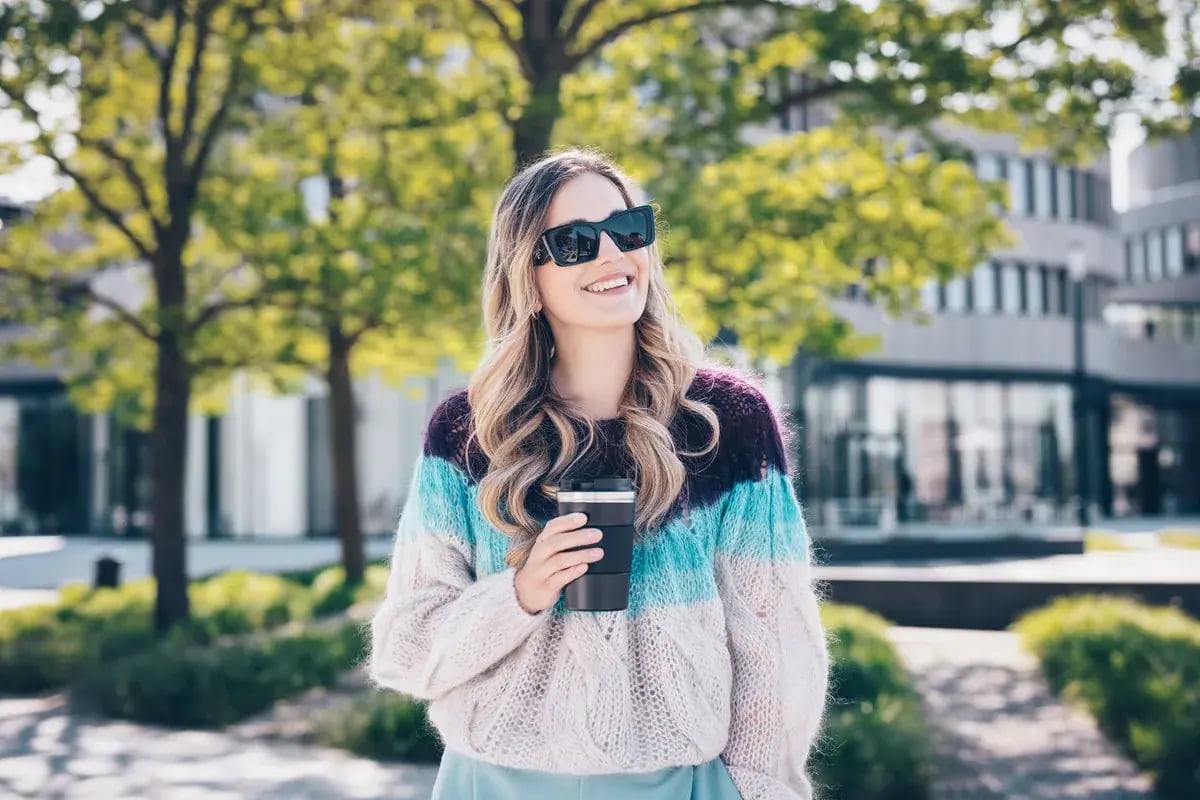 Frau mit schwarzer Sonnenbrille hält einen Coffee-to-go-Becher im Freien