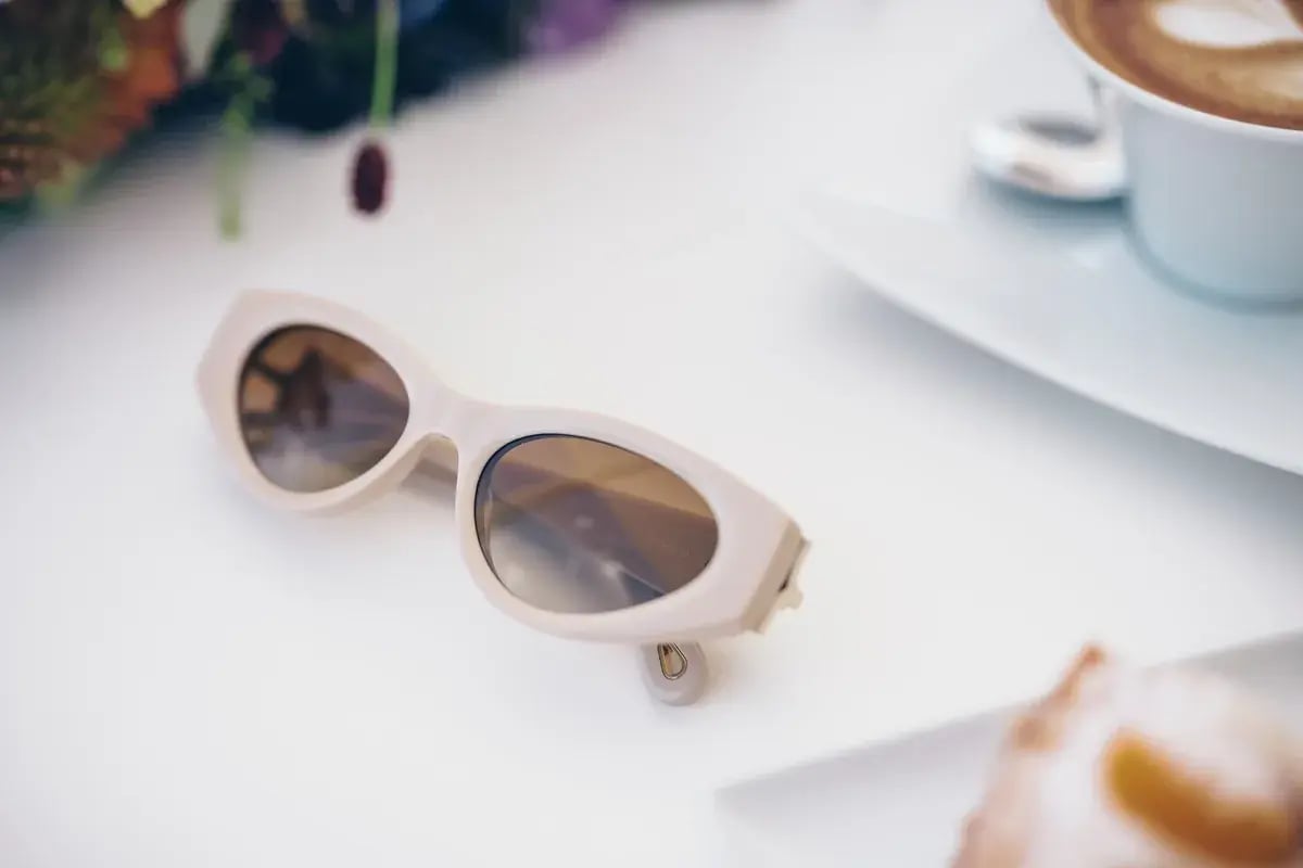 Beige Sonnenbrille liegt auf weißem Tisch neben Kaffeetasse