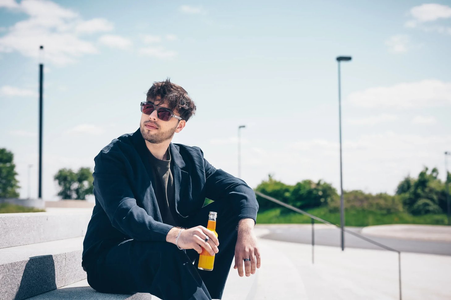 Mann mit dunkler Sonnenbrille sitzt auf Stufen und hält eine Getränkeflasche
