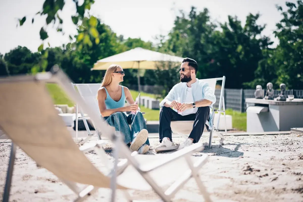 Paar mit Sonnenbrillen sitzt auf Liegestühlen im Freien und unterhält sich