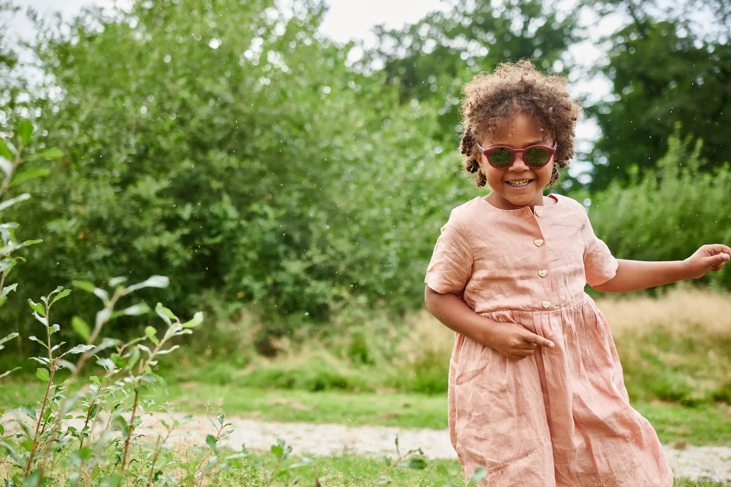 Kleines Mädchen mit rosa Sonnenbrille läuft lachend im Grünen