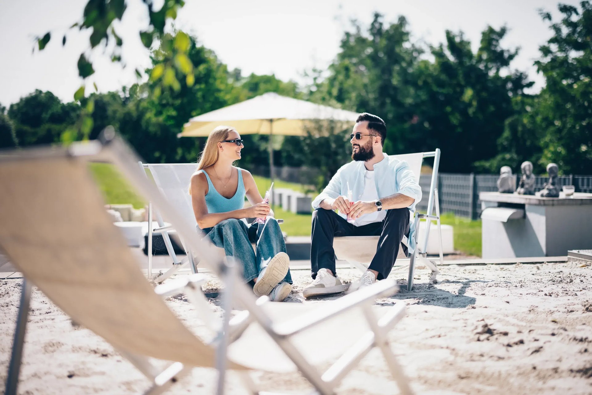 Paar mit Sonnenbrillen sitzt auf Liegestühlen im Freien und unterhält sich