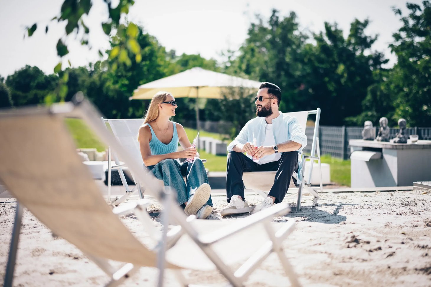 Paar mit Sonnenbrillen sitzt auf Liegestühlen im Freien und unterhält sich