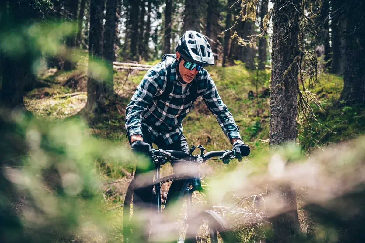 Mann mit Helm und Sportbrille fährt auf einem Mountainbike durch den Wald