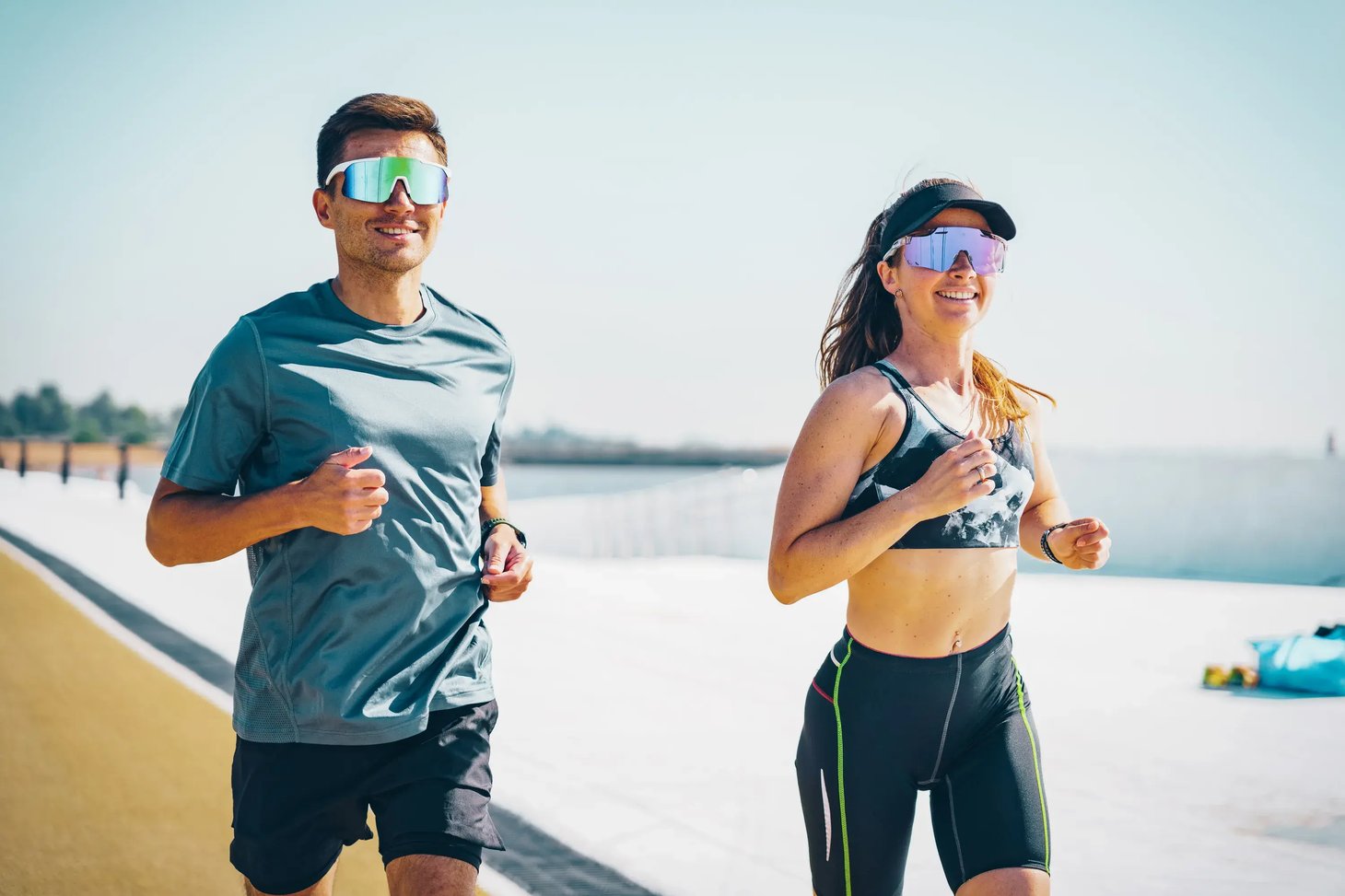 Mann und Frau mit Sportbrillen laufen lächelnd auf einer Promenade nebeneinander
