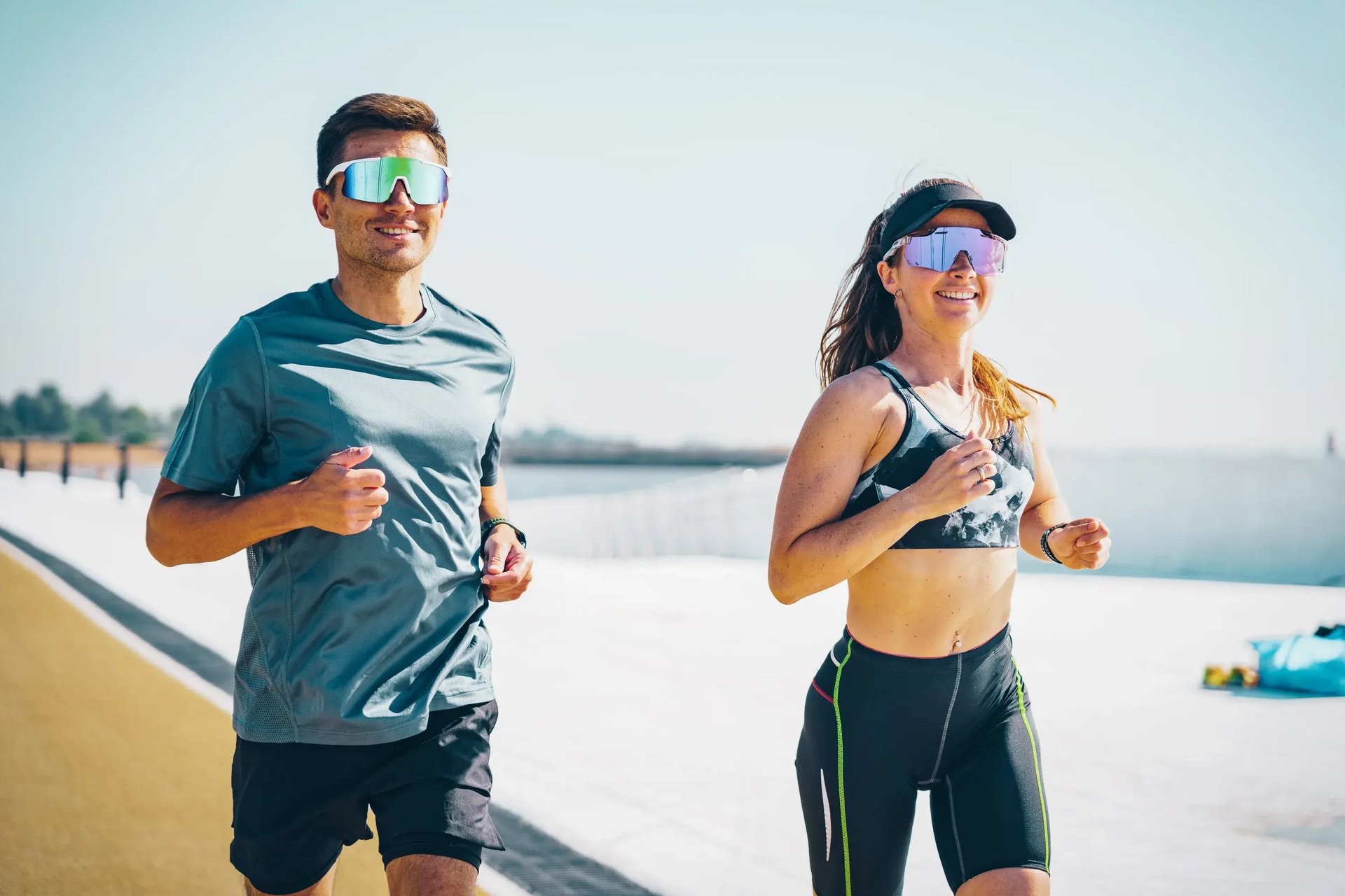 Mann und Frau mit Sportbrillen laufen lächelnd auf einer Promenade nebeneinander