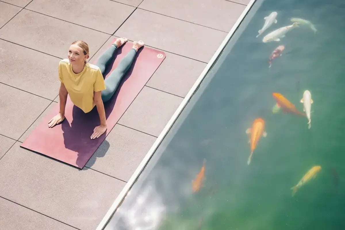 Frau macht Yoga auf einer Matte neben einem Teich mit Koi-Karpfen