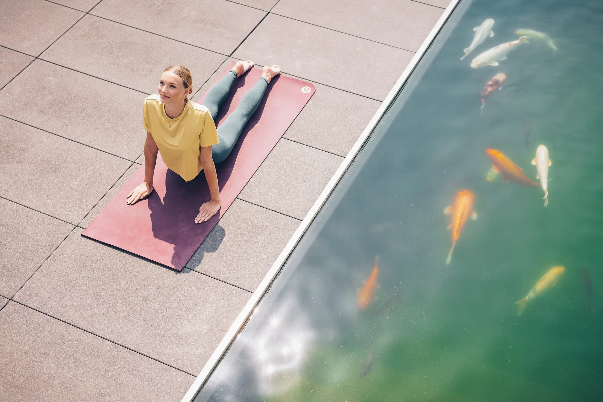 Frau in Kobra-Yoga-Pose auf Matte neben einem Teich mit Koi-Fischen