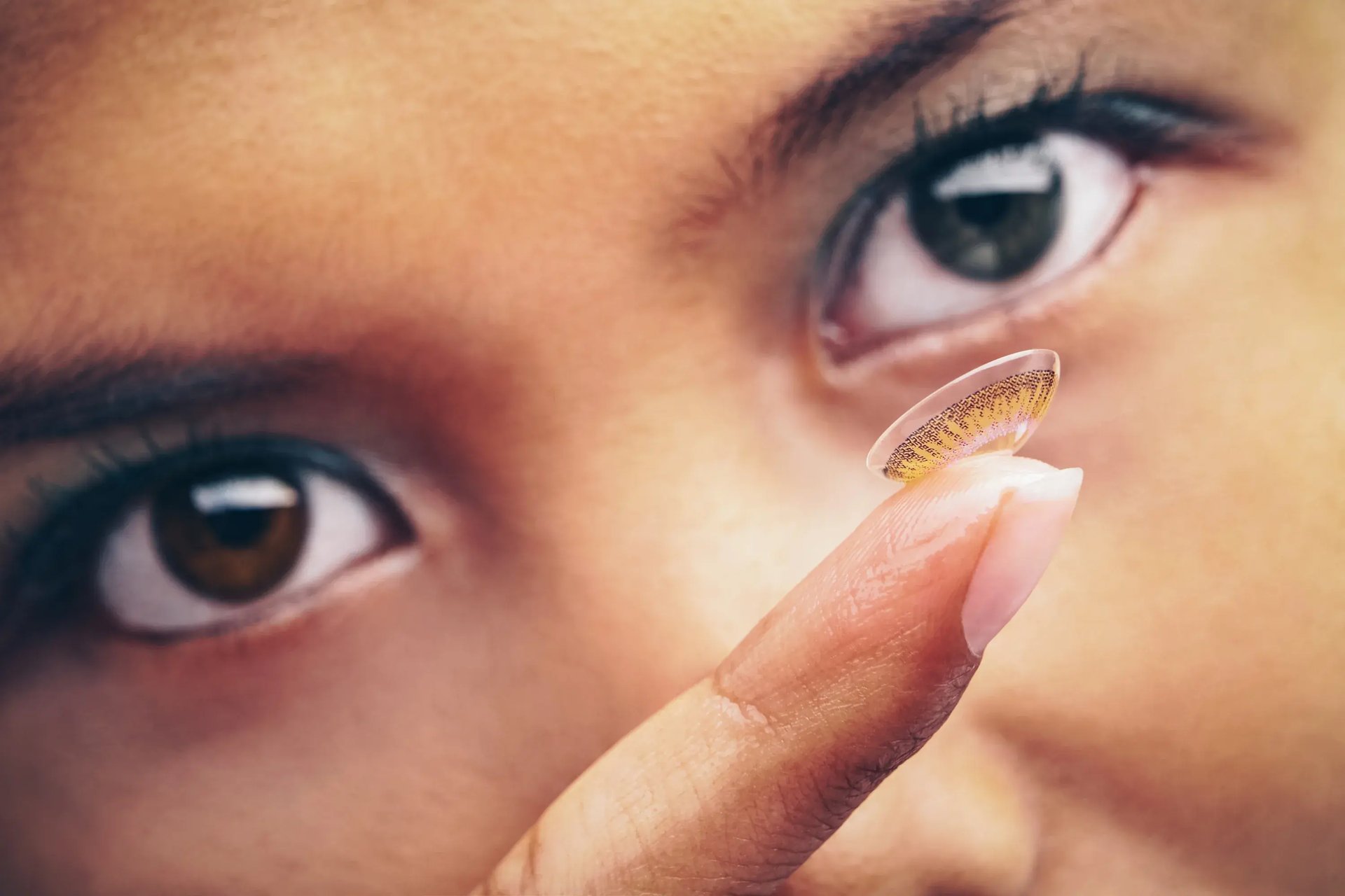 Person hält eine farbige Kontaktlinse auf dem Finger vor braune Augen
