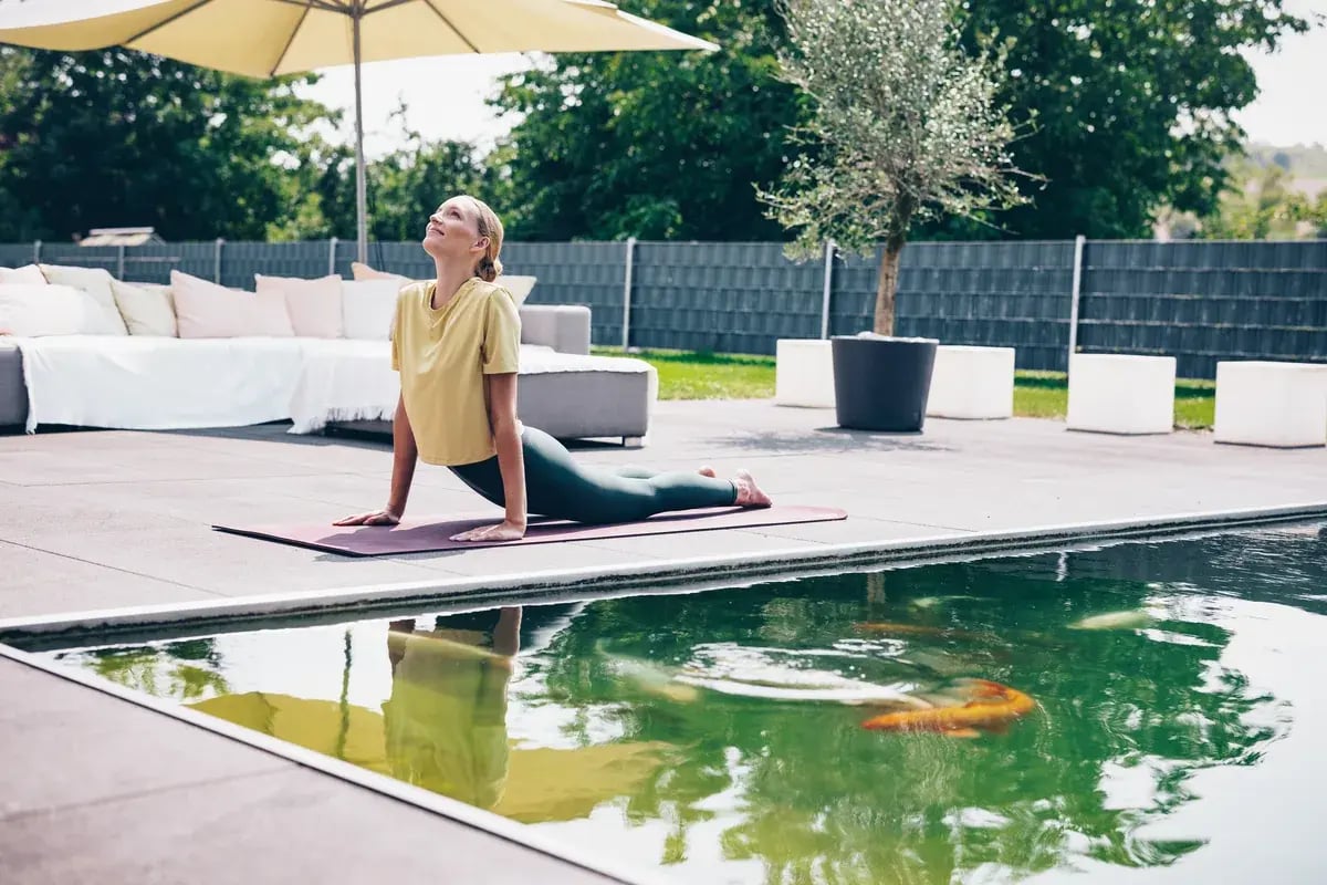 Frau in Kobra-Yoga-Pose auf Matte an einem Teich mit Koi-Fischen