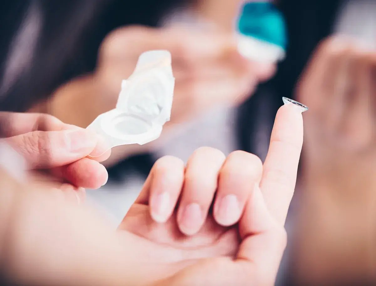 Hand hält geöffnete Kontaktlinsenverpackung, auf Finger liegt eine Kontaktlinse