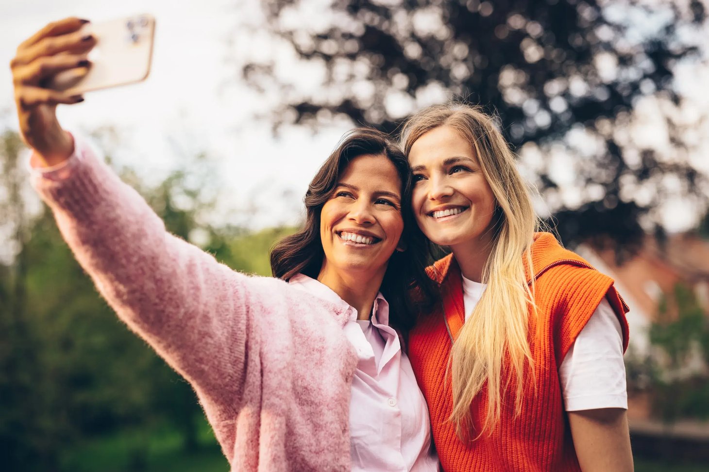 Zwei Frauen machen lächelnd ein Selfie mit Smartphone im Freien