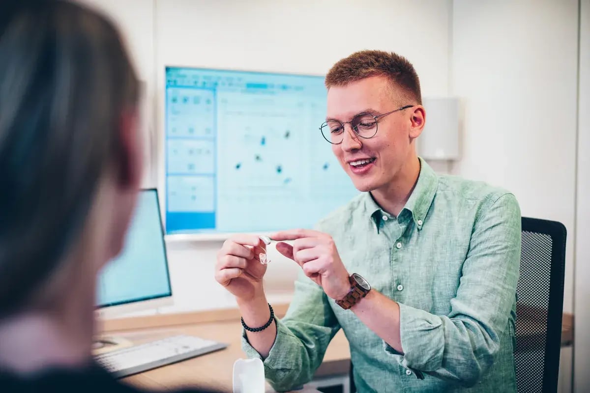 Mann mit Brille zeigt einer Person ein kleines transparentes Objekt in einem Beratungsraum