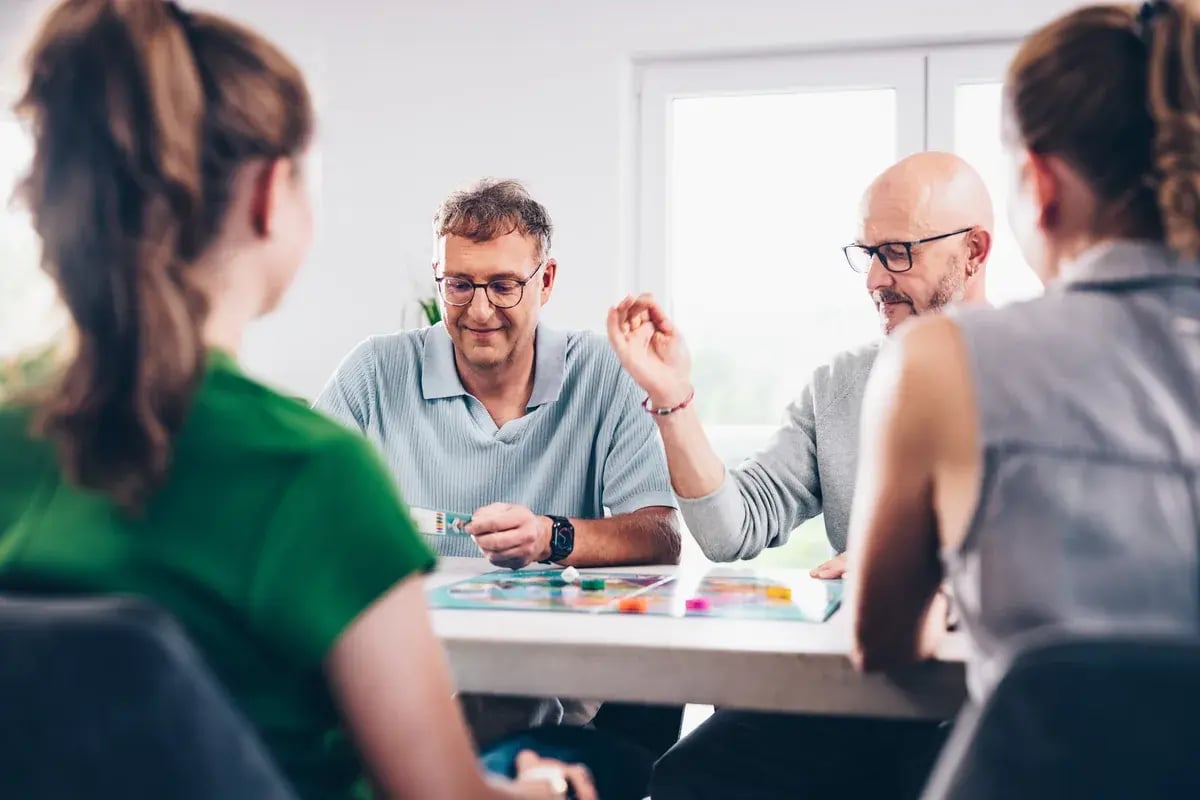 Vier Personen sitzen an einem Tisch und spielen gemeinsam ein Brettspiel