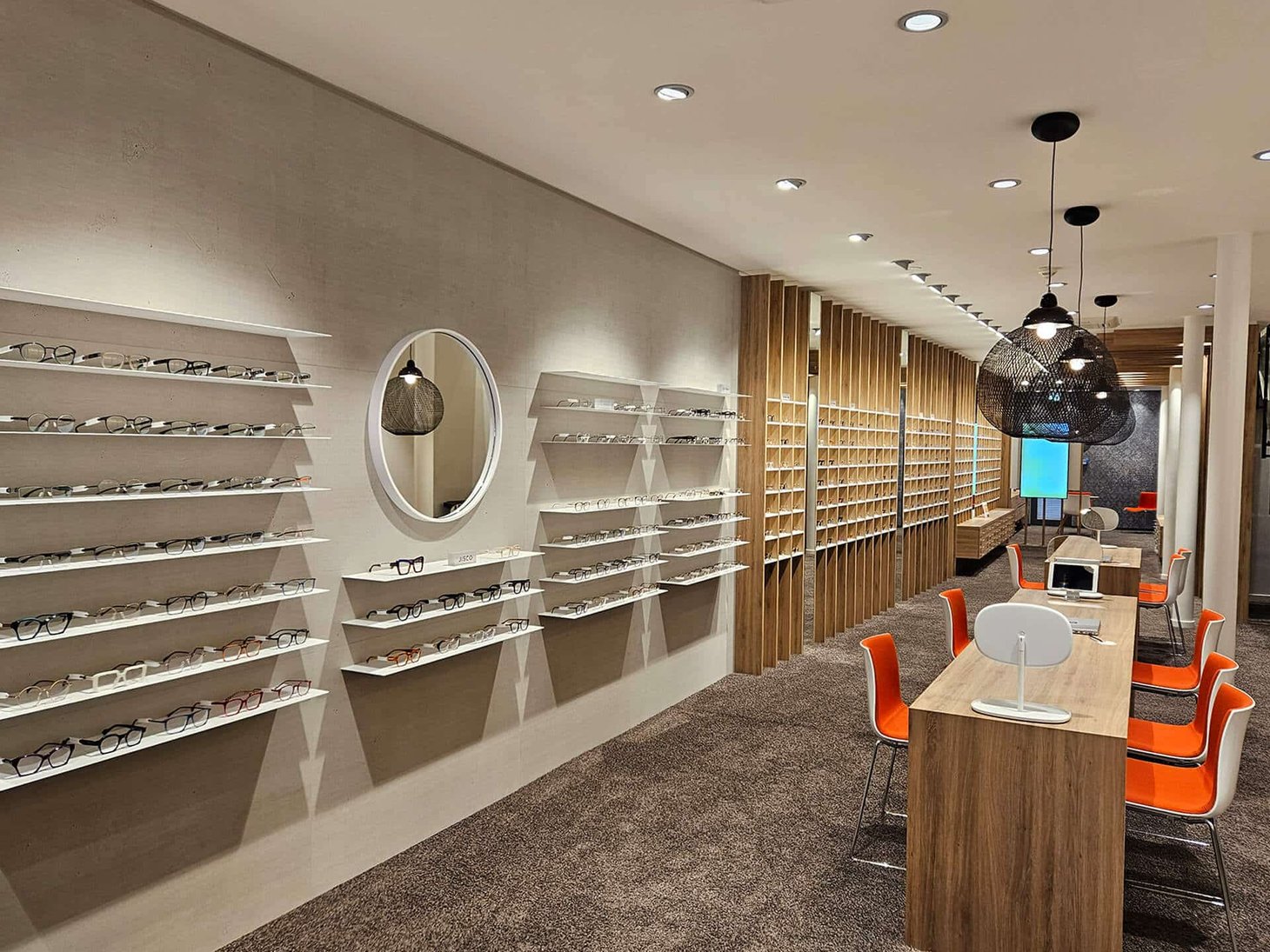 Optiker-Innenraum mit holzvertäfeltem Brillenregal, Beratungstisch und Laptop