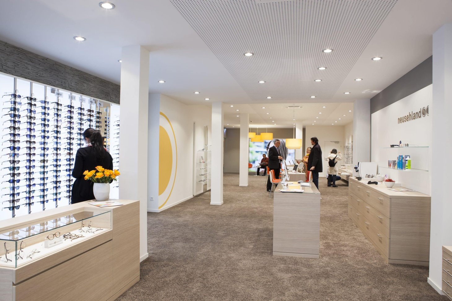 Mehrere Personen in einem hellen Optiker-Geschäft vor Brillenregalen und Tresen
