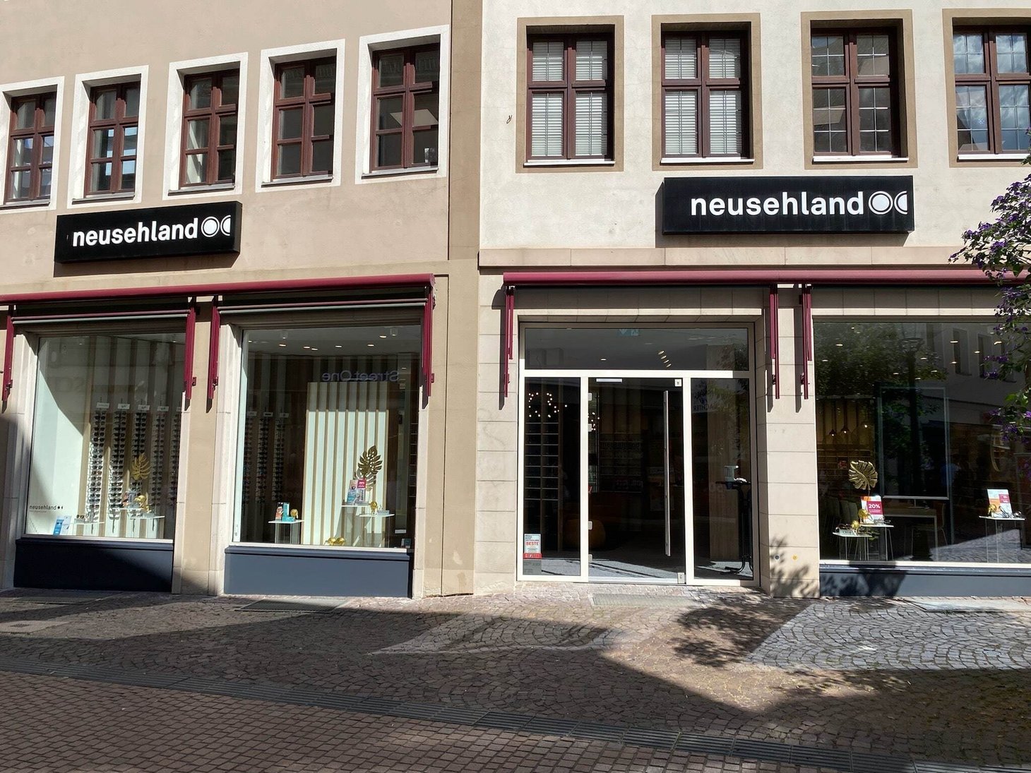Ladenfront mit zwei Schriftzügen "neusehland" auf heller Fassade, Fußgängerzone