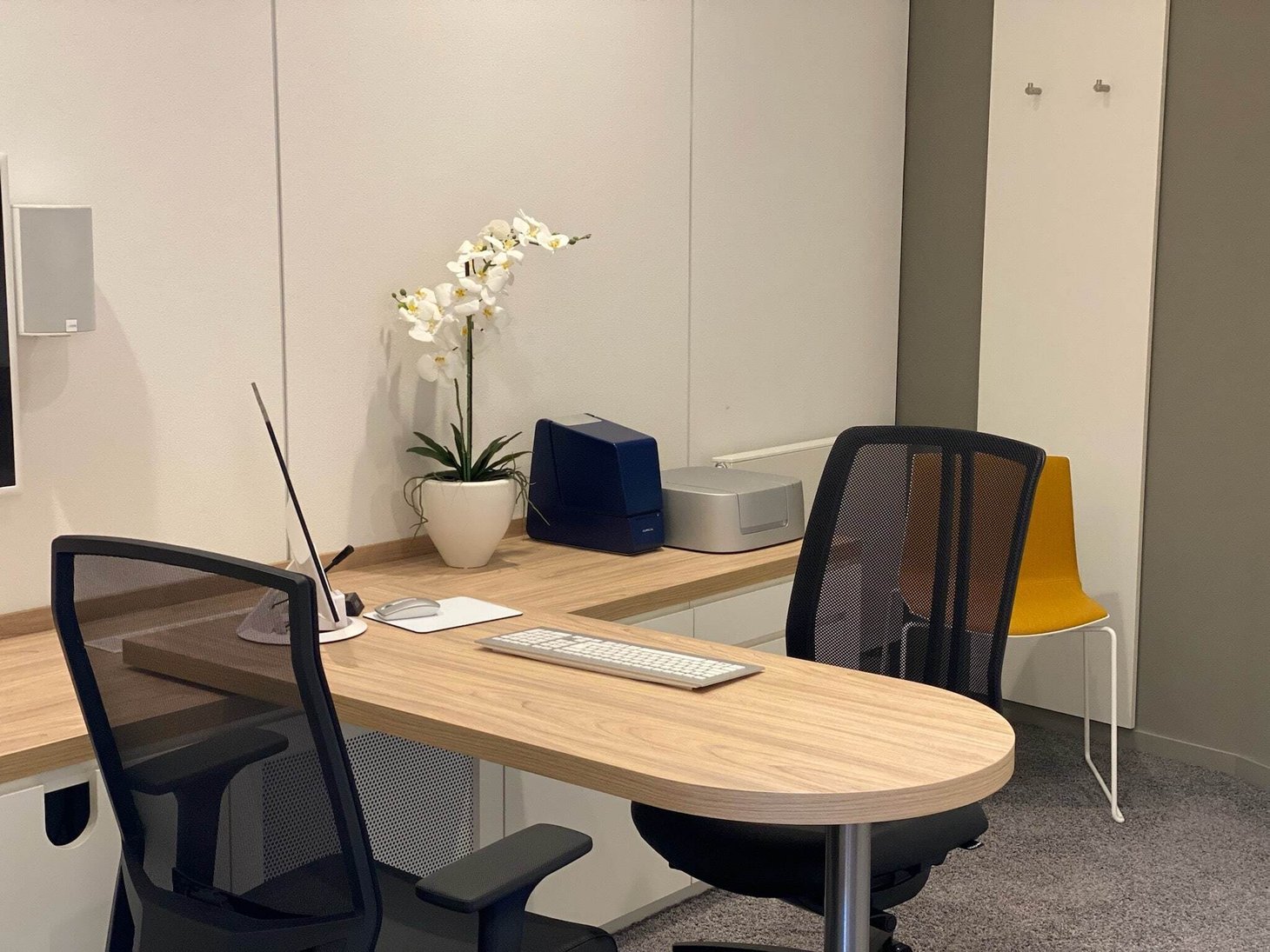 Leerer Beratungsraum mit zwei Schreibtischstühlen, Holztisch, Tastatur und weißer Orchidee