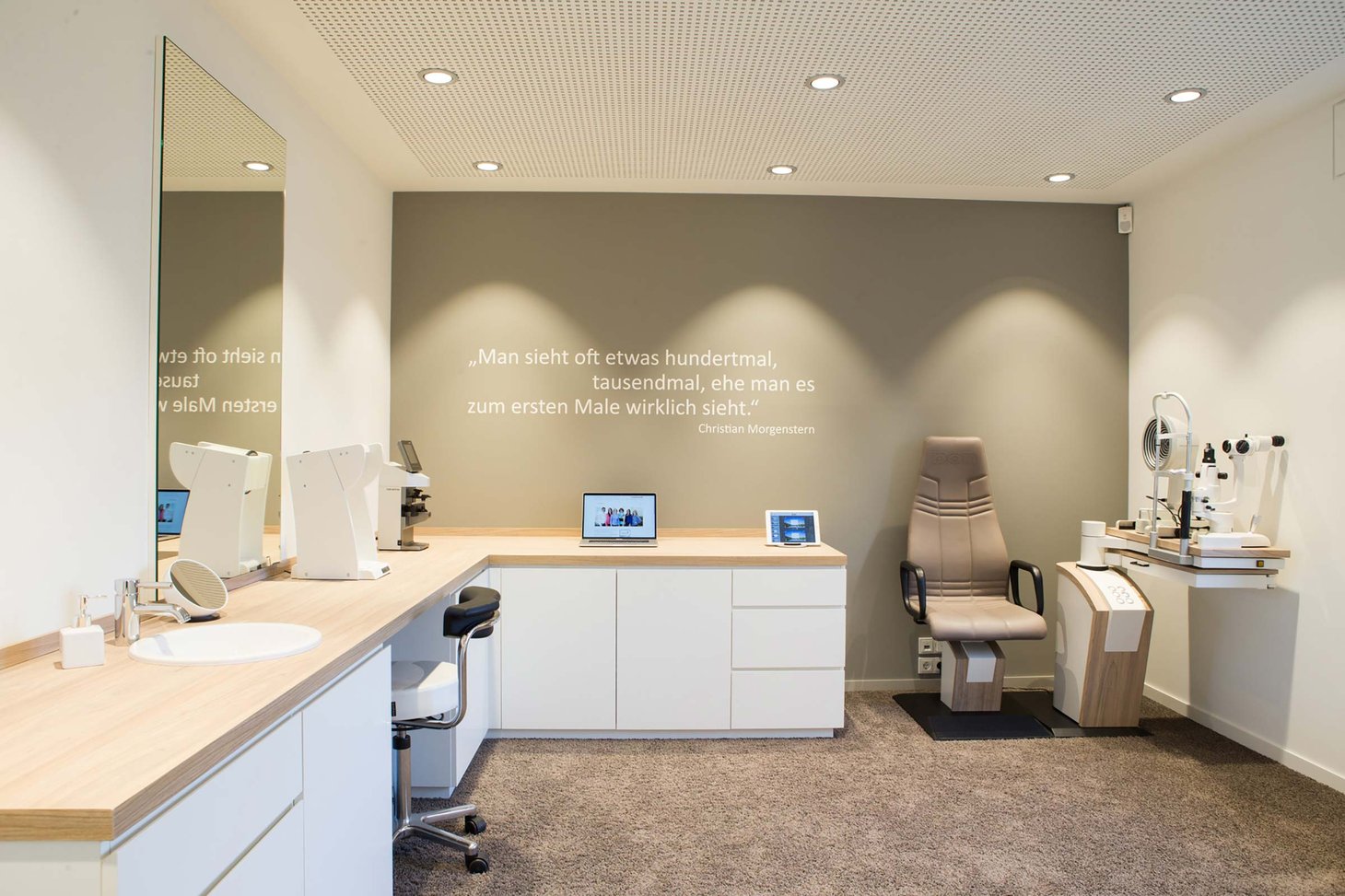 Untersuchungsraum mit Spaltlampe, Patientenstuhl und Zitat von Christian Morgenstern an der Wand