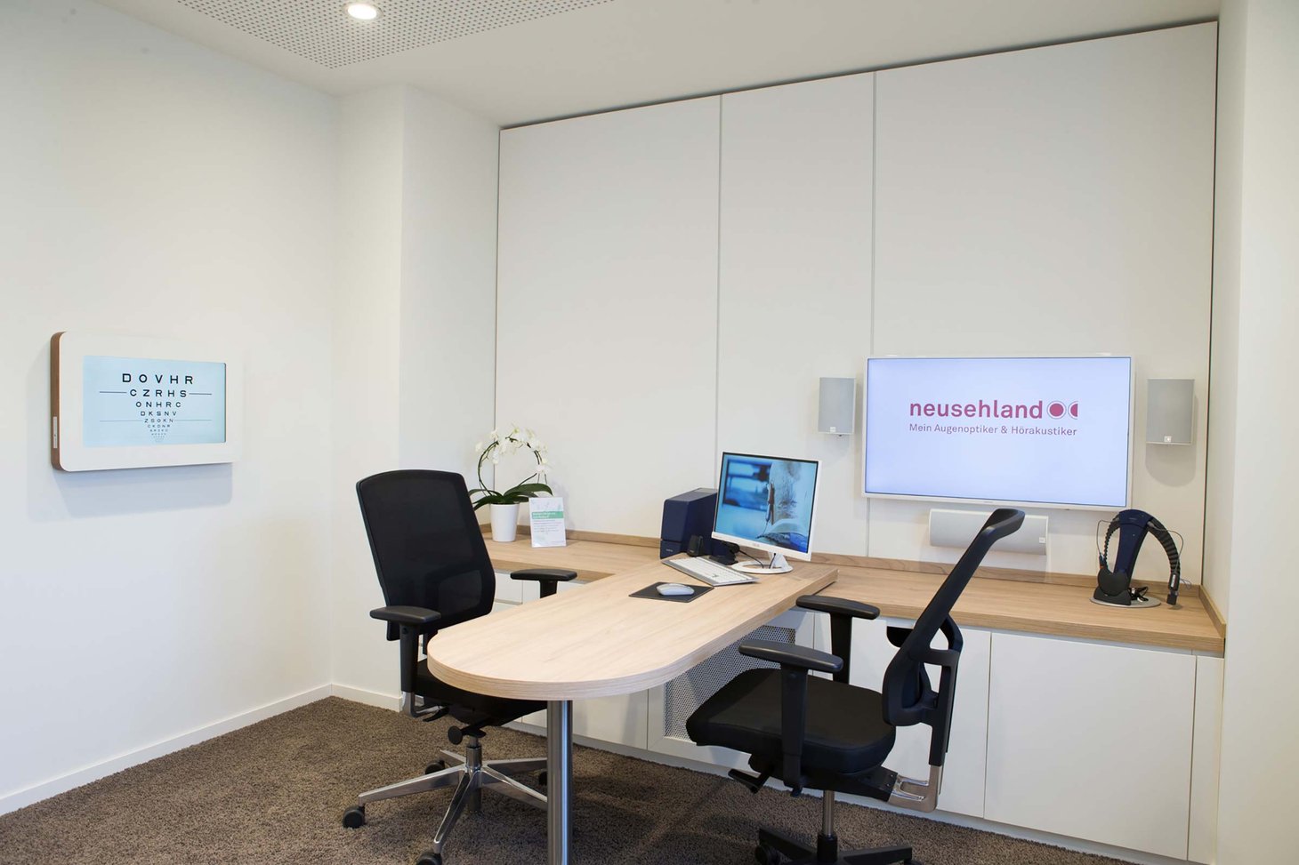 Kleiner Beratungsraum mit rundem Tisch, zwei Bürostühlen, Monitor und Wandbildschirm