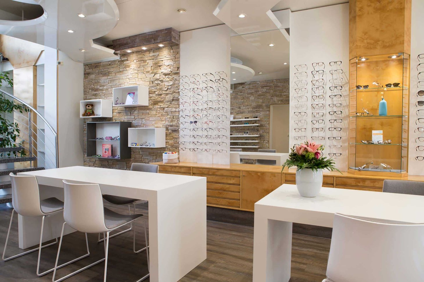 Optiker-Innenraum mit Natursteinwand, Brillenregalen und zwei weißen Beratungstischen
