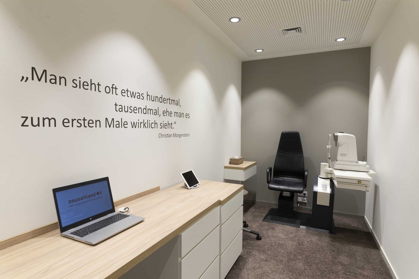 Untersuchungsraum mit Spaltlampe, Patientenstuhl und Zitat von Christian Morgenstern an der Wand