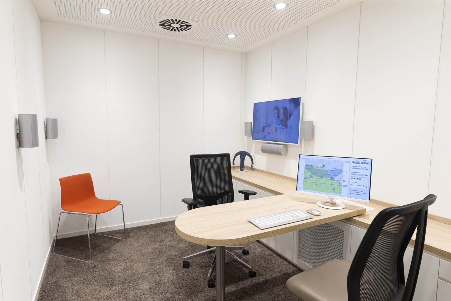Kleiner Beratungsraum mit rundem Tisch, zwei Bürostühlen, Monitor und Wandbildschirm